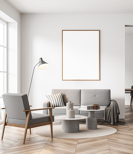 Jasny salon z szarą sofą, fotelem, okrągłymi stolikami i lampą stojącą przy oknie