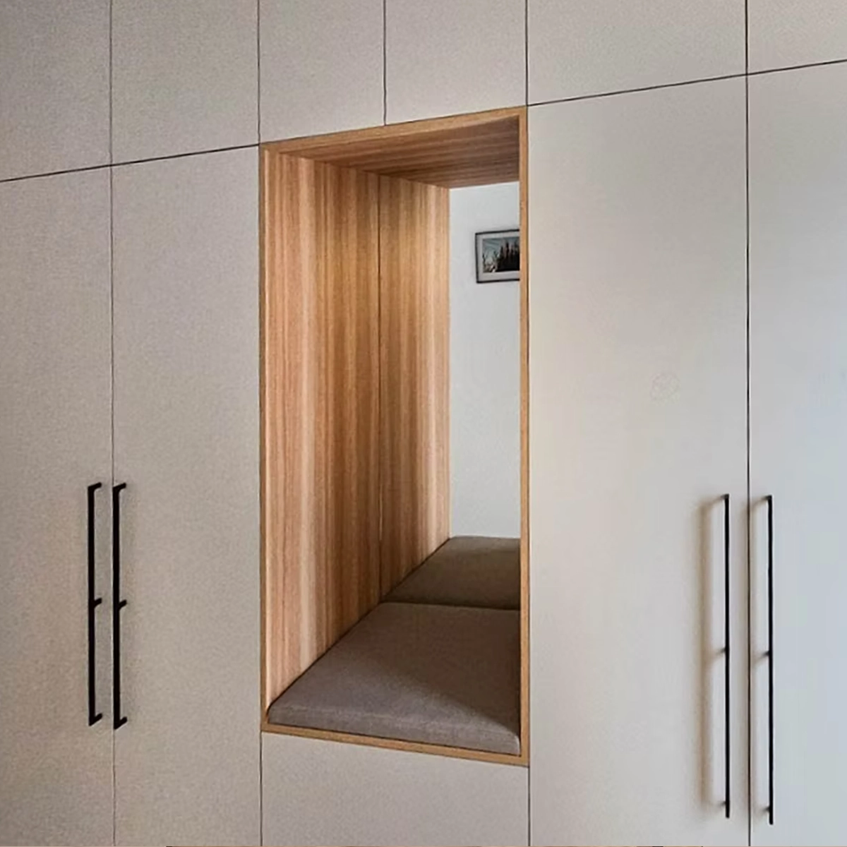 Deckenhohe Schrankwand im Flur mit cremefarbenen Fronten und langen schwarzen Griffleisten; in der Mitte eine mit Holz ausgekleidete offene Nische mit gepolsterter Sitzbank.